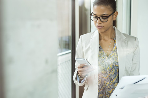 Junge Frau im Büro mit Mobiltelefon, lizenzfreies Stockfoto