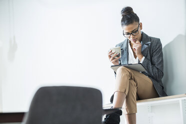 Junge Frau im Büro mit einer Tasse Kaffee und einem digitalen Tablet - UUF005800