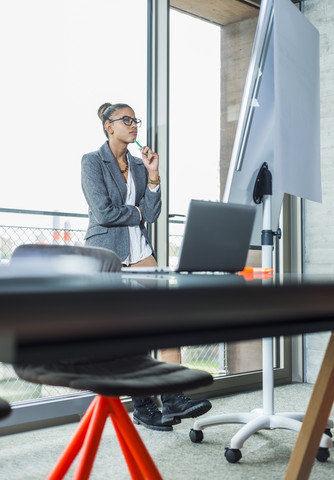 Junge Frau im Büro schaut auf Flipchart, lizenzfreies Stockfoto