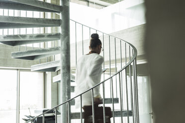 Young woman in office walking up spiral staircase - UUF005806