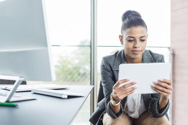 Junge Frau im Büro schaut auf ein digitales Tablet - UUF005826