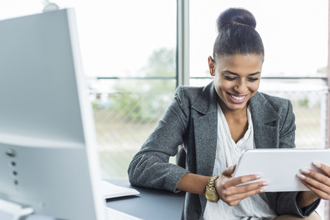Lächelnde junge Frau im Büro, die auf ein digitales Tablet schaut, lizenzfreies Stockfoto
