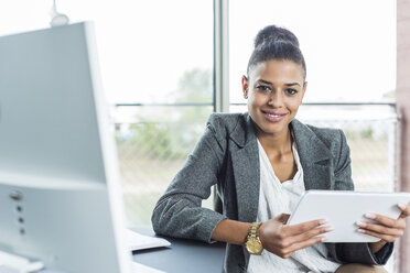 Portrait of smiling young woman in office holding digital tablet - UUF005828