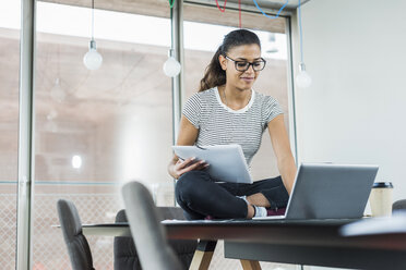 Smiling young woman sitting on conference table using laptop - UUF005835