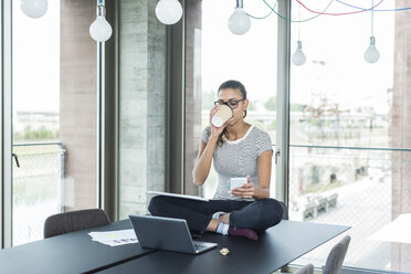 Young woman sitting on conference table looking at cell phone - UUF005836