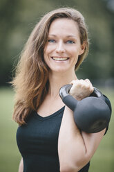 Smiling woman holding kettlebell - MADF000531