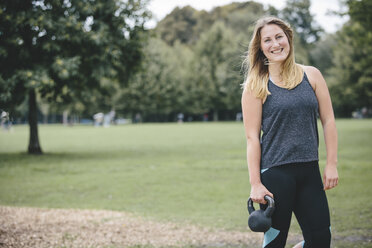 Lächelnde junge Frau hält Kettlebell im Park - MADF000555