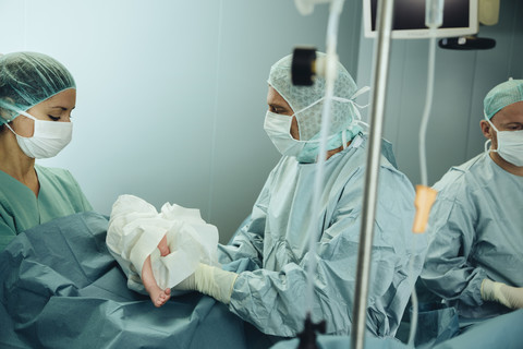 Surgeon handing over newborn to operating room nurse after c-section stock photo