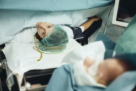 Krankenschwester im Operationssaal bringt Baby nach Kaiserschnitt zur Mutter, lizenzfreies Stockfoto