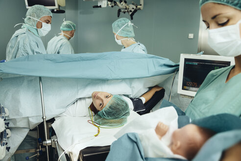 Operating room nurse bringing baby to mother while team finishing c-section - MFF002359