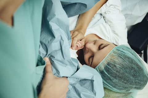 Mutter berührt die Hand ihres Neugeborenen direkt nach dem Kaiserschnitt, lizenzfreies Stockfoto