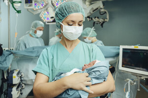 Operating room nurse holding newborn in operating room - MFF002366