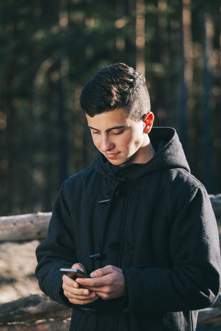 Schwarz gekleideter Jugendlicher, der eine SMS auf seinem Mobiltelefon schreibt, lizenzfreies Stockfoto