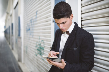 Young man wearing jacket and a wooden bow tie using digital tablet - RAEF000549