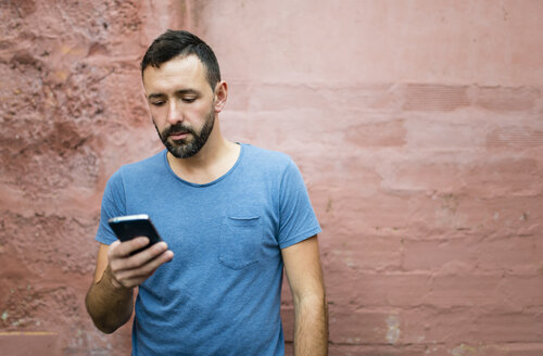Porträt eines bärtigen Mannes, der auf sein Smartphone schaut - RAEF000554