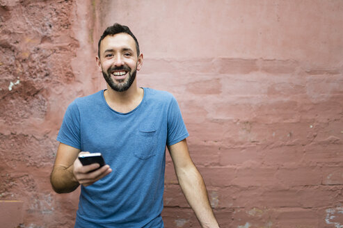 Porträt eines lächelnden, bärtigen Mannes mit Smartphone - RAEF000555