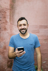 Portrait of smiling bearded man with smartphone - RAEF000556