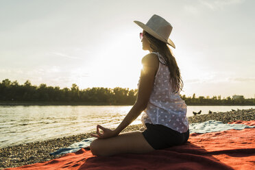 Junge Frau übt Yoga am Flussufer bei Sonnenuntergang - UUF005900