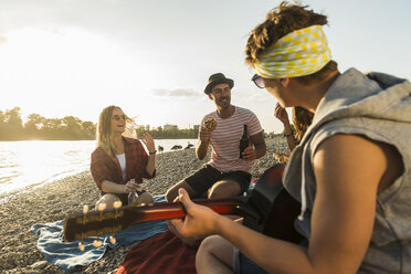 Friends with guitar relaxing at the riverside at sunset - UUF005904