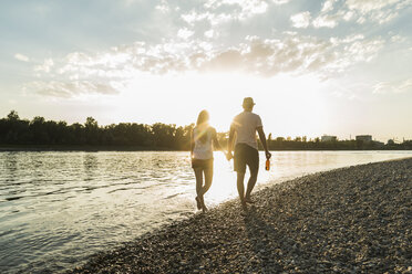 Paar spaziert Hand in Hand am Ufer des Flusses bei Sonnenuntergang - UUF005913