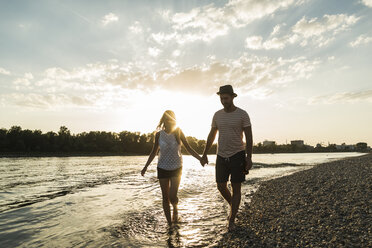 Couple walking hand in hand at the riverside at sunset - UUF005914