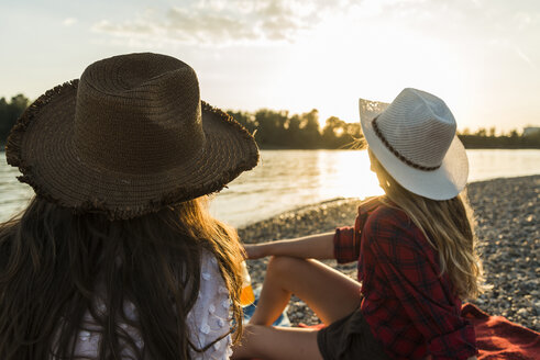 Zwei Freunde mit Strohhüten entspannen sich bei Sonnenuntergang am Flussufer - UUF005918