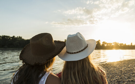 Zwei Freunde mit Strohhüten entspannen sich bei Sonnenuntergang am Flussufer - UUF005919