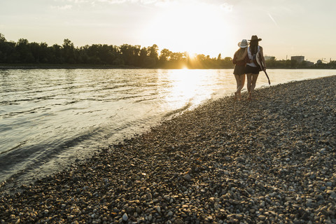 Zwei Freunde gehen bei Sonnenuntergang am Flussufer spazieren, lizenzfreies Stockfoto