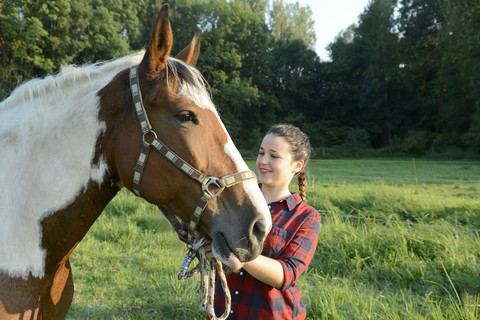 Junge Frau steht auf einem Feld und hält ihr Pferd, lizenzfreies Stockfoto