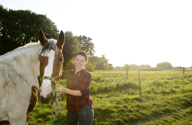 Junge Frau steht auf einem Feld und hält ihr Pferd - BFRF001553