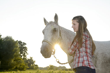 Junge Frau steht auf einem Feld und hält ihr Pferd - BFRF001556