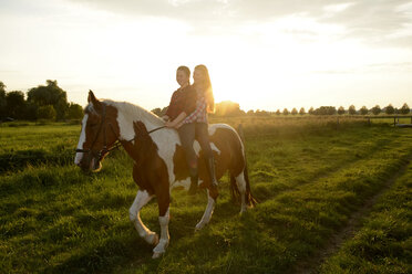 Junge Frauen reiten in einem Feld bei Sonnenuntergang - BFRF001568