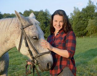 Junge Frau steht auf einem Feld und hält ihr Pferd - BFRF001572