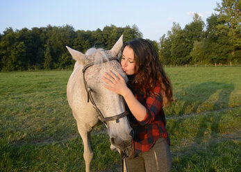 Junge Frau steht auf einem Feld und hält ihr Pferd - BFRF001573