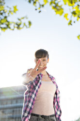 Smiling young woman showing victory sign at evening twilight - FKF001394