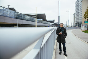 Österreich, Wien, Mann steht auf einer Fahrbahn in der Nähe des Hauptbahnhofs und schaut auf sein Smartphone - AIF000104