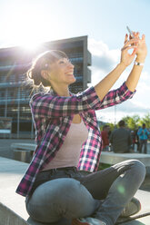 Germany, Berlin, portrait of happy young woman taking a selfie with smartphone - FKF001410