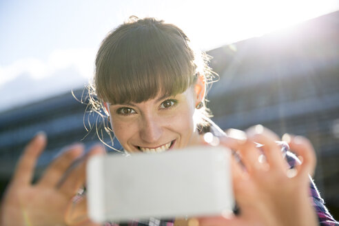Porträt einer lächelnden jungen Frau, die mit einem Smartphone fotografiert - FKF001423
