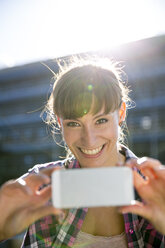 Porträt einer lächelnden jungen Frau, die mit einem Smartphone fotografiert - FKF001426