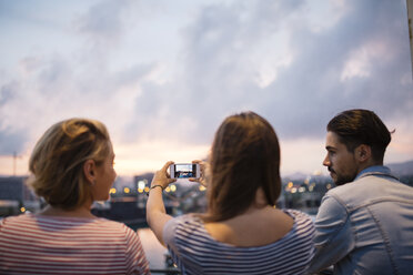 Spain, Barcelona, back view of three friends taking a picture of view with smartphone - JRFF000153