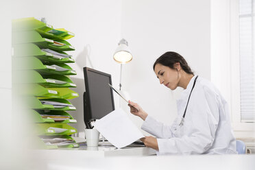 Doctor sitting at desk looking at document - FKF001448