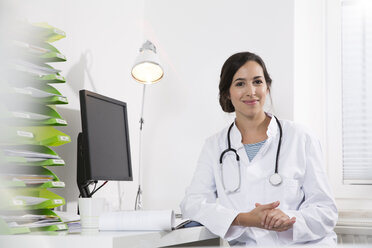 Portrait of smiling doctor sitting at desk - FKF001449