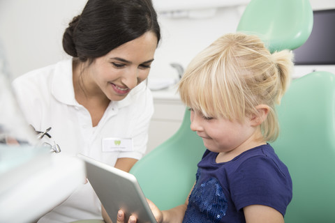 Zahnarzt und lächelndes Mädchen mit digitalem Tablet im Zahnarztstuhl, lizenzfreies Stockfoto
