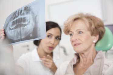 Dentist explaining x-ray image to senior woman in dentist's chair - FKF001478