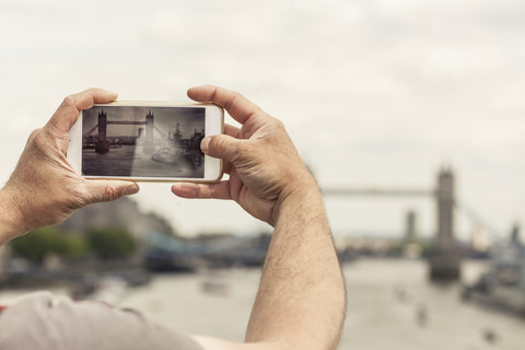 UK, London, Mann fotografiert die Tower Bridge mit seinem Smartphone, lizenzfreies Stockfoto