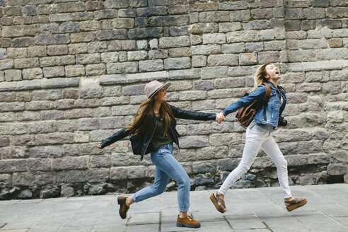 Spain, Barcelona, two young women running hand in hand in the city - EBSF000939