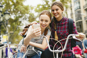 Spanien, Barcelona, zwei junge Frauen mit Handy und Fahrrädern in der Stadt - EBSF000974