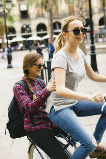 Spanien, Barcelona, zwei glückliche junge Frauen teilen sich ein Fahrrad in der Stadt - EBSF000979