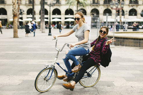Spanien, Barcelona, zwei glückliche junge Frauen teilen sich ein Fahrrad in der Stadt - EBSF000981