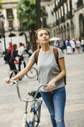 Spain, Barcelona, young woman pushing bicycle in the city - EBSF000986